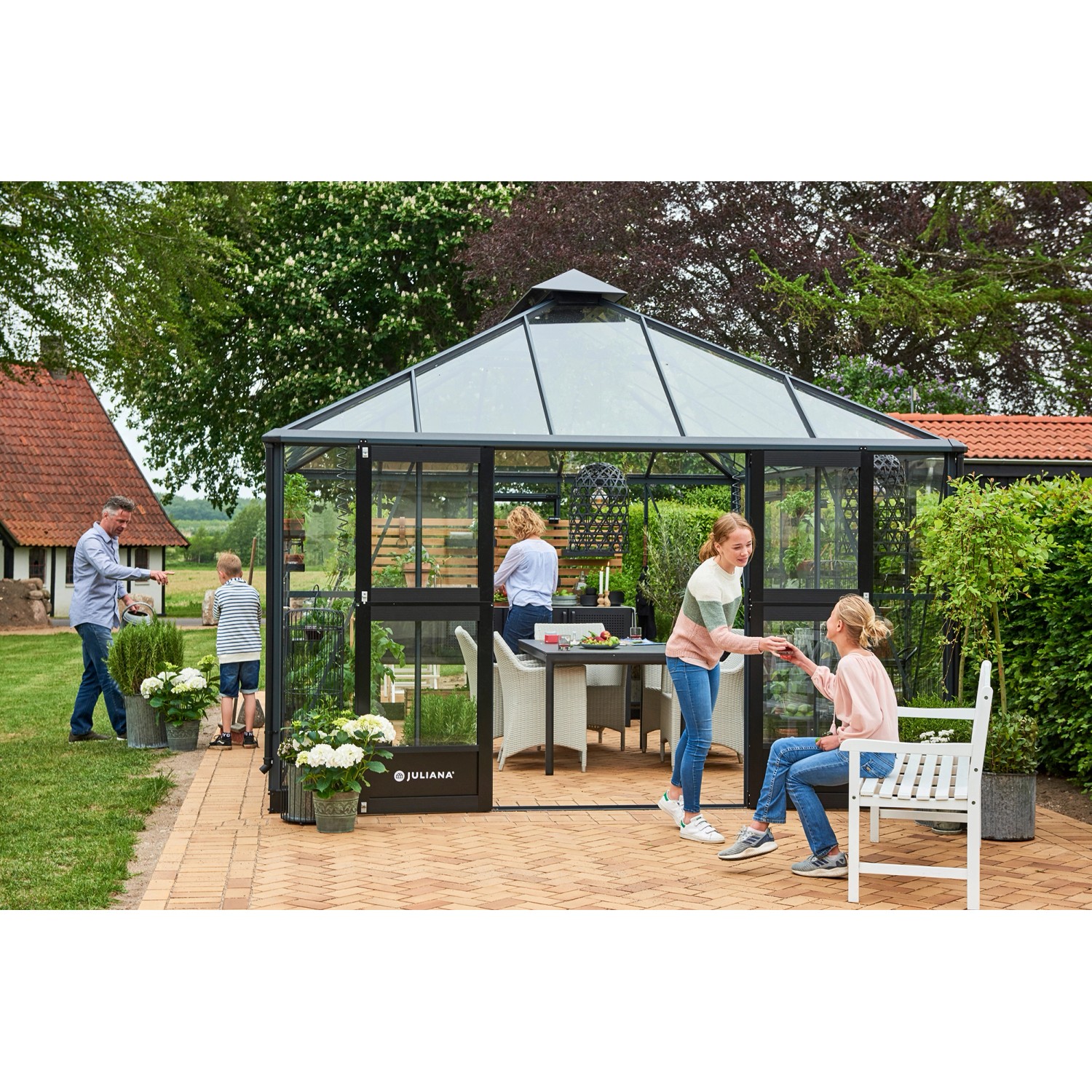 Juliana Gewächshaus Grand Oase 18, anthrazit-schwarz, mit Familie im Garten. Begehbares Glas-Gewächshaus mit Fundamentrahmen.
