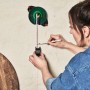 Frau benutzt Bosch Atino Linienlaser mit Maßband an Wand zur Ausrichtung.