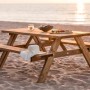 Axi Picknicktisch Julie aus Holz, braun, mit Speisen und Hut am Strand.