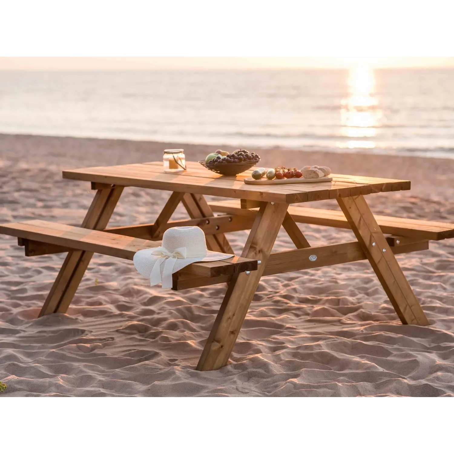 Axi Picknicktisch Julie aus Holz, braun, mit Speisen und Hut am Strand.