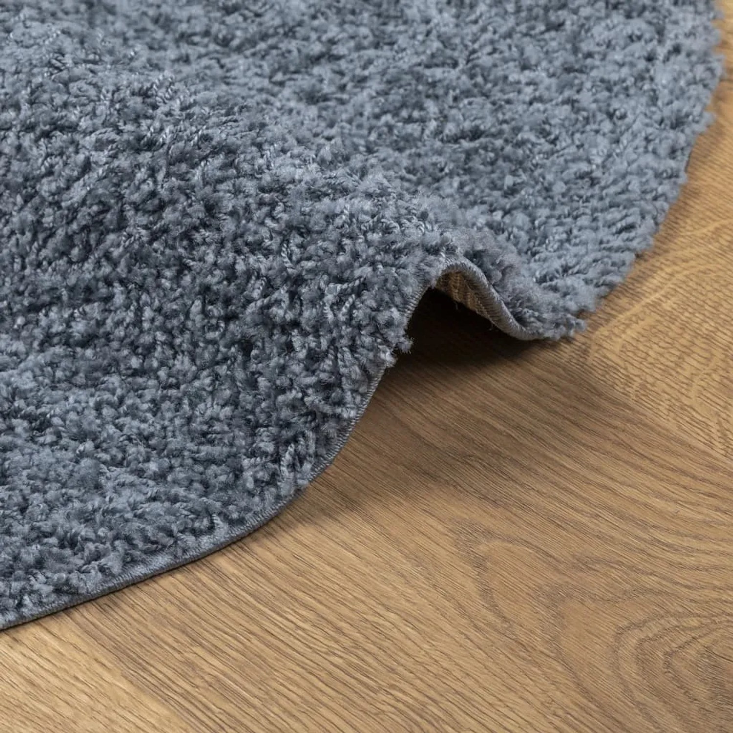 Blauer, runder Shaggy Teppich (Ø 200 cm) mit hochflorigem Flor auf Holzboden.