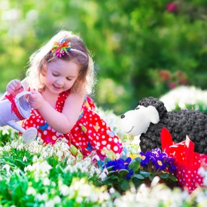 Schwarze Keramik Gartenfigur Schaf mit lächelndem Gesicht im Blumenbeet, Kind gießt Blumen. Wetterfeste Dekofigur.