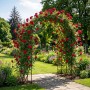 Schwarzer Rosenbogen aus Eisen, bewachsen mit roten Rosen, als Rankhilfe im Garten.