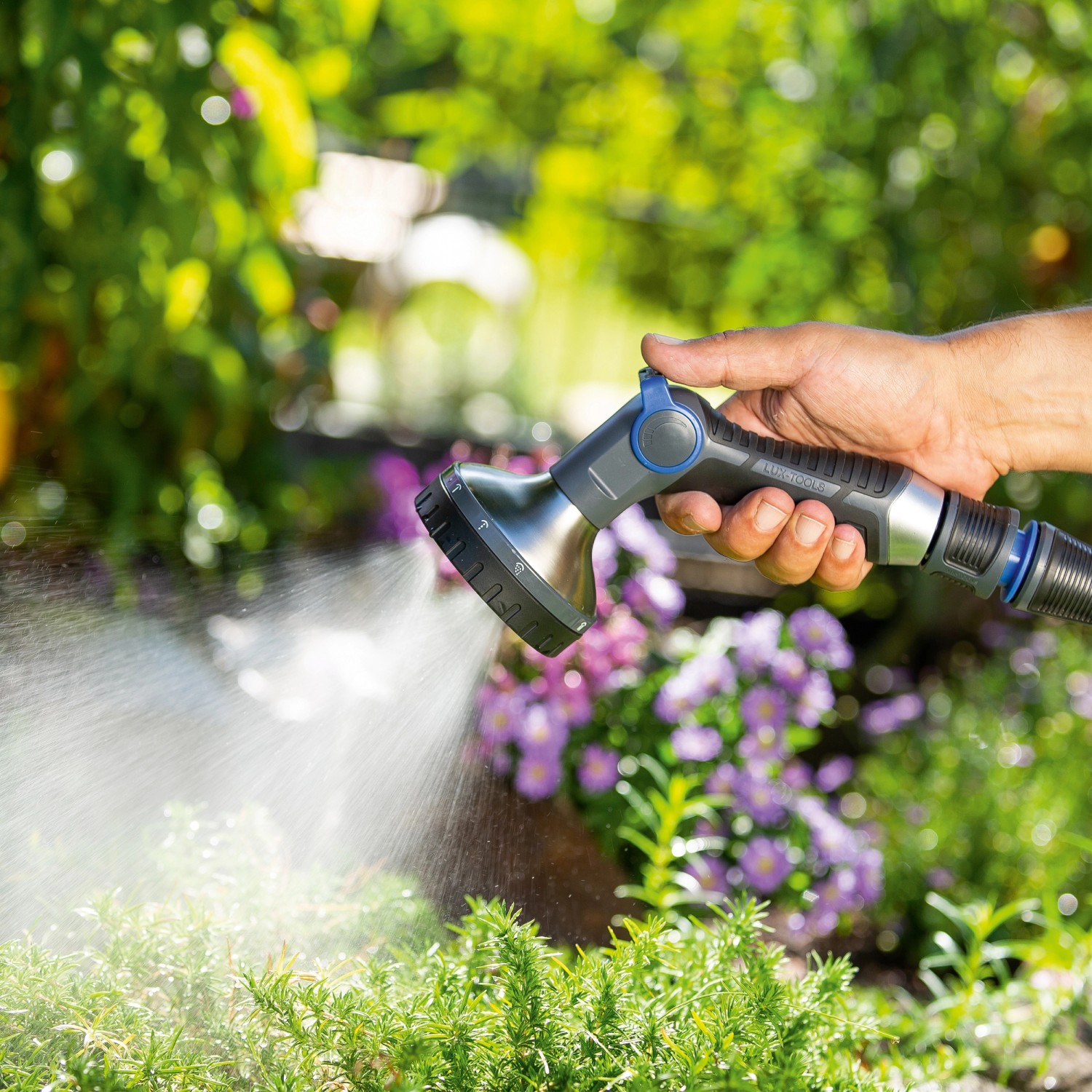 Hand hält LUX Multifunktionsbrause mit 10 Strahlvarianten beim Bewässern von Pflanzen.