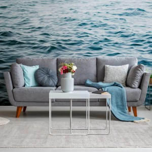 Fototapete Maritim in Blau-Weiß hinter grauem Sofa mit Deko. PROFHOME Vliestapete mit Meeresmotiv.