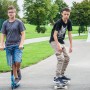 Zwei Jugendliche mit blauem Six Degrees Stuntscooter und Skateboard im Skatepark.