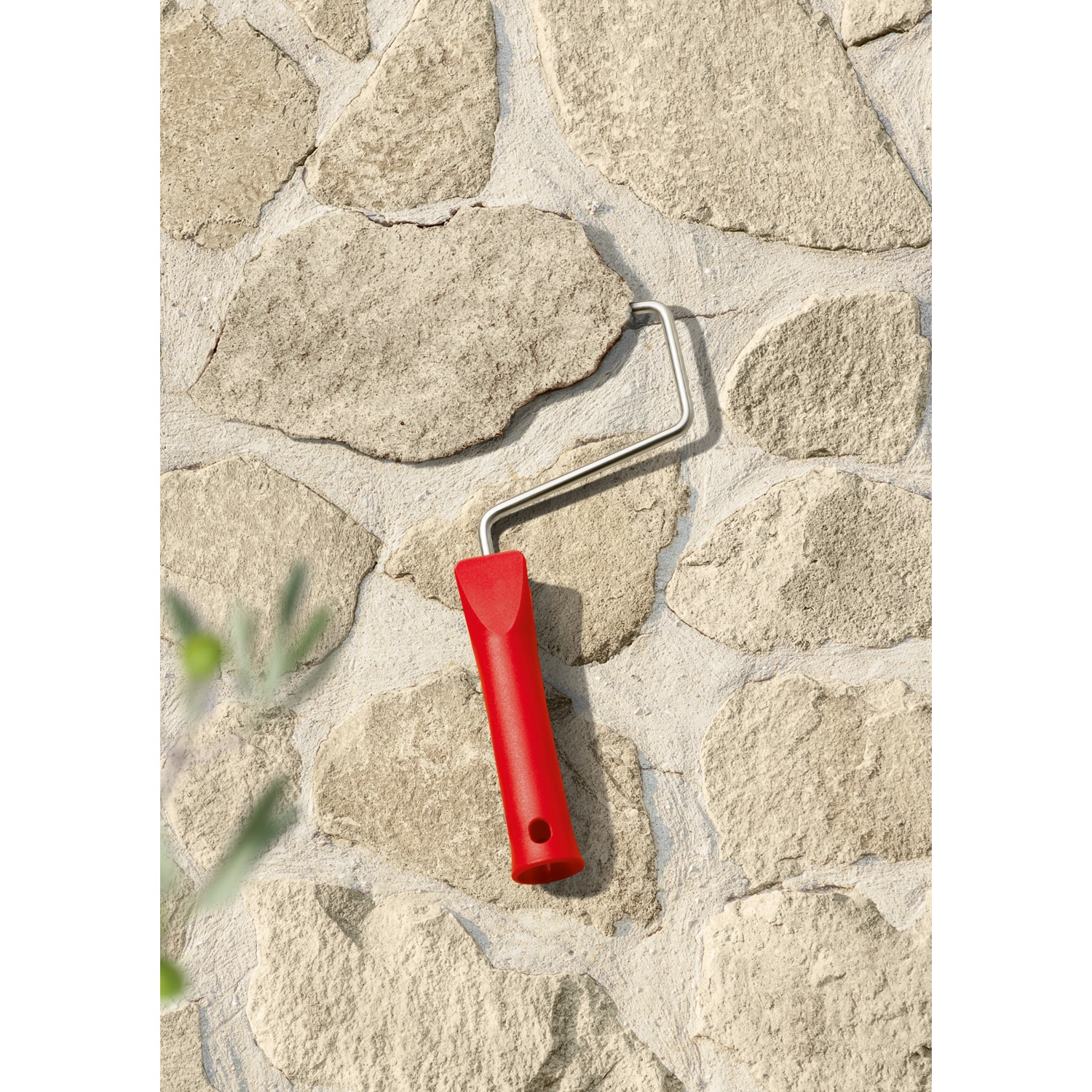 Farbroller mit rotem Griff vor einer mit Schöner Wohnen Trendfarbe Finca gestrichenen Wand.