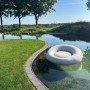 Anthrazitfarbenes, aufblasbares Best Daybed Rondo im Wasser, umgeben von Grünflächen.