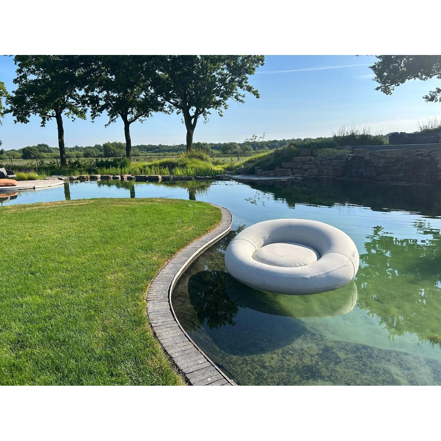 Anthrazitfarbenes, aufblasbares Best Daybed Rondo im Wasser, umgeben von Grünflächen.