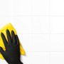 Hand mit schwarzem Einmalhandschuh (Größe L) und gelbem Tuch beim Reinigen weißer Fliesen.