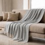 Hellgraue The White Stone Sofadecke aus Baumwoll-Mix, 130x170 cm, mit Fransen auf beigem Sofa.