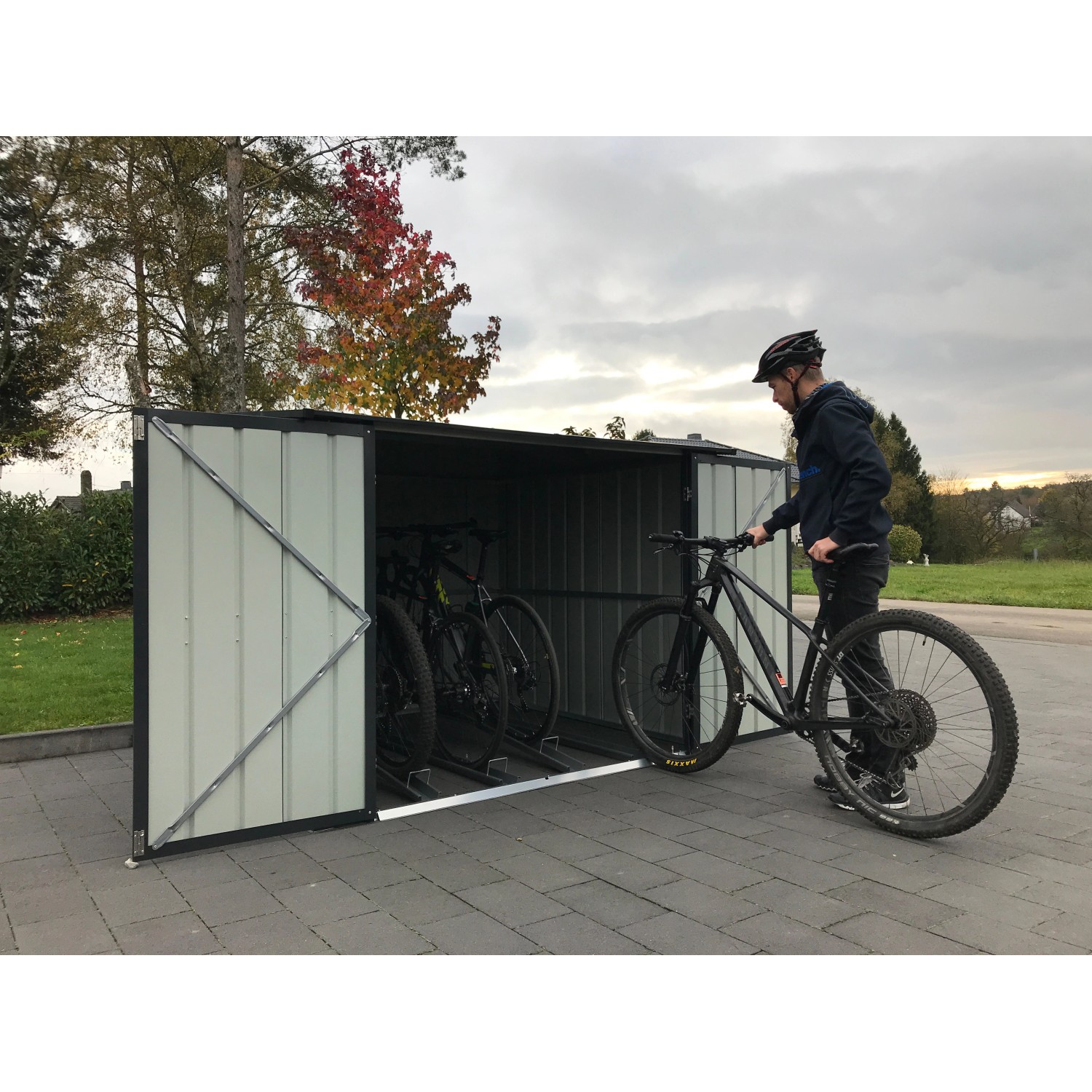 Anthrazitfarbene Globel Fahrradbox Family mit 4 Fahrradhaltern und einer Person mit Fahrrad.