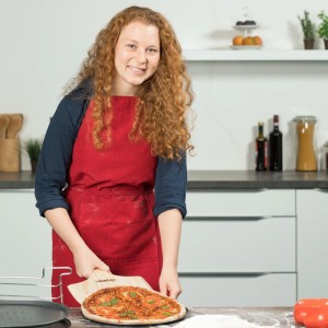 Lachende Frau hält Relaxdays Pizzaschieber aus Kiefernholz mit belegter Pizza in moderner Küche.