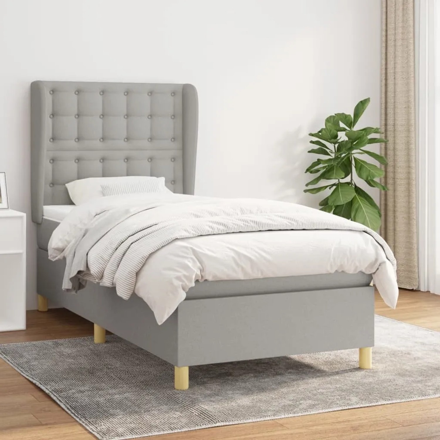 Helles, graues Boxspringbett 90x190 cm mit Matratze und Stoffbezug im Schlafzimmer.