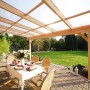 Skan Holz Terrassenüberdachung Ravenna aus Douglasie mit Polycarbonatplatten, darunter ein gedeckter Tisch.