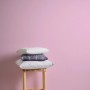 Rosa Kinderzimmer Vliestapete Uni, mit Kissen auf Hocker vor der Tapete.