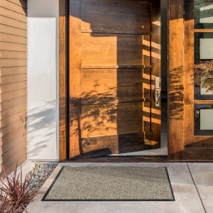 Karat Schmutzfangmatte SKY, ocker-schwarz, 135x200 cm vor einer Holztür.