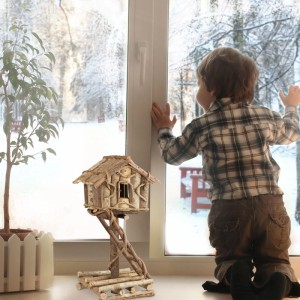 Handgefertigtes Vogelhaus aus Naturholz auf rustikalem Pfahl mit Leiter, als Deko auf Fensterbank im Winter.