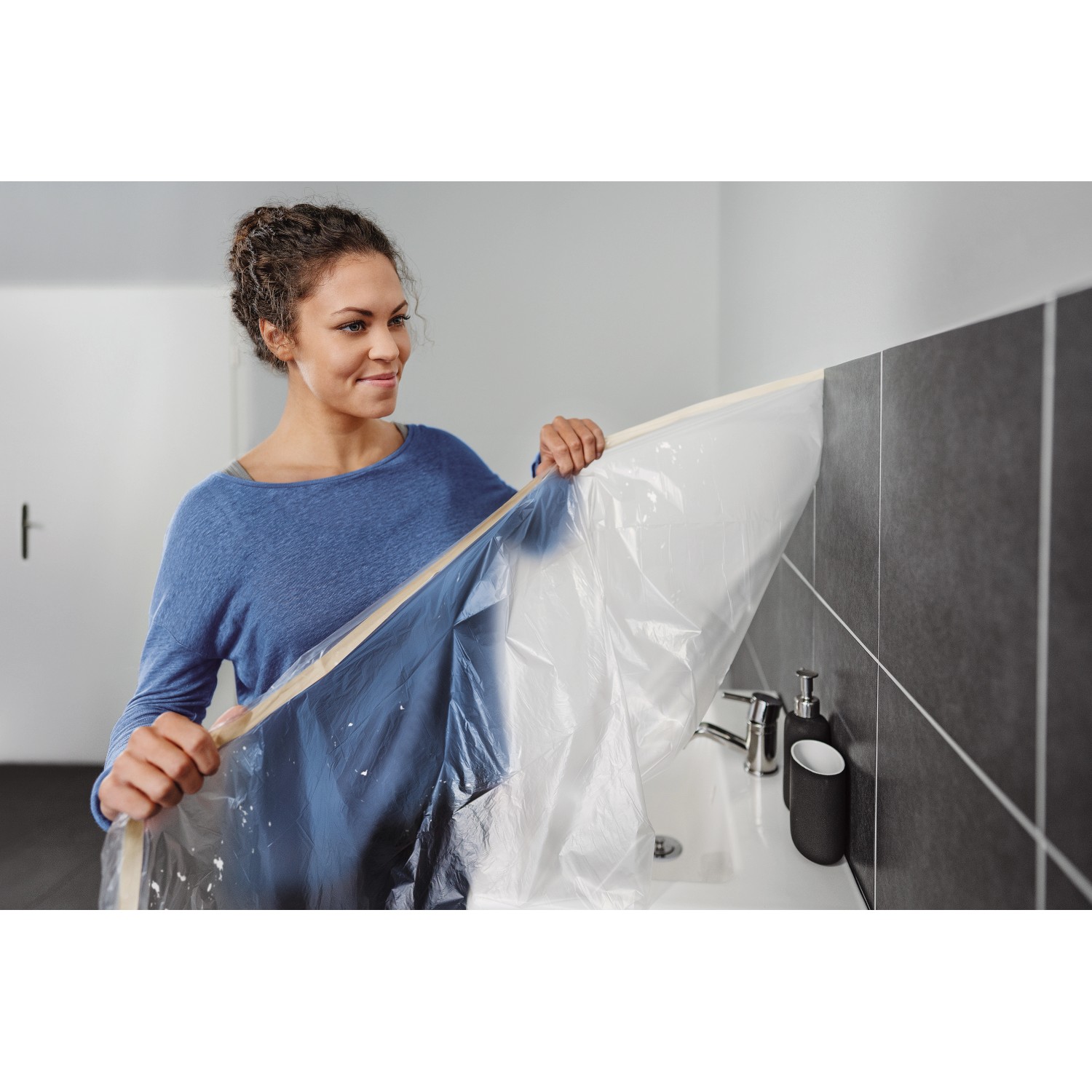 Frau befestigt Tesa Abdeckfolie mit Klebeband im Bad. Easy Cover Economy M Nachfüllung.