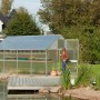 KGT Gewächshaus Orchidee Alu blank 12,74 m² mit geöffneter Tür und Frau im Garten.