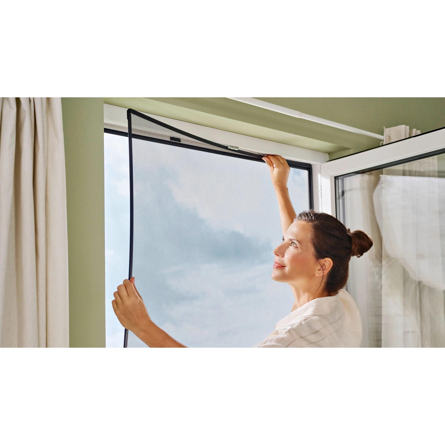 Frau montiert tesa® Insect Stop Anklips-Rahmen (anthrazit) am Fenster. Insektenschutz für Fenster.