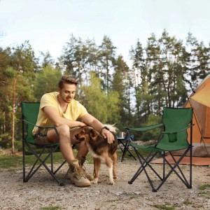 Zwei grüne Sunula Campingstühle mit Mann und Hund vor Zelt. Faltbare Anglerstühle mit Getränkehalter.