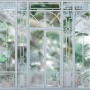 Komar Fototapete Orangerie, 368x254 cm, mit Pflanzen hinter Glasfassade.
