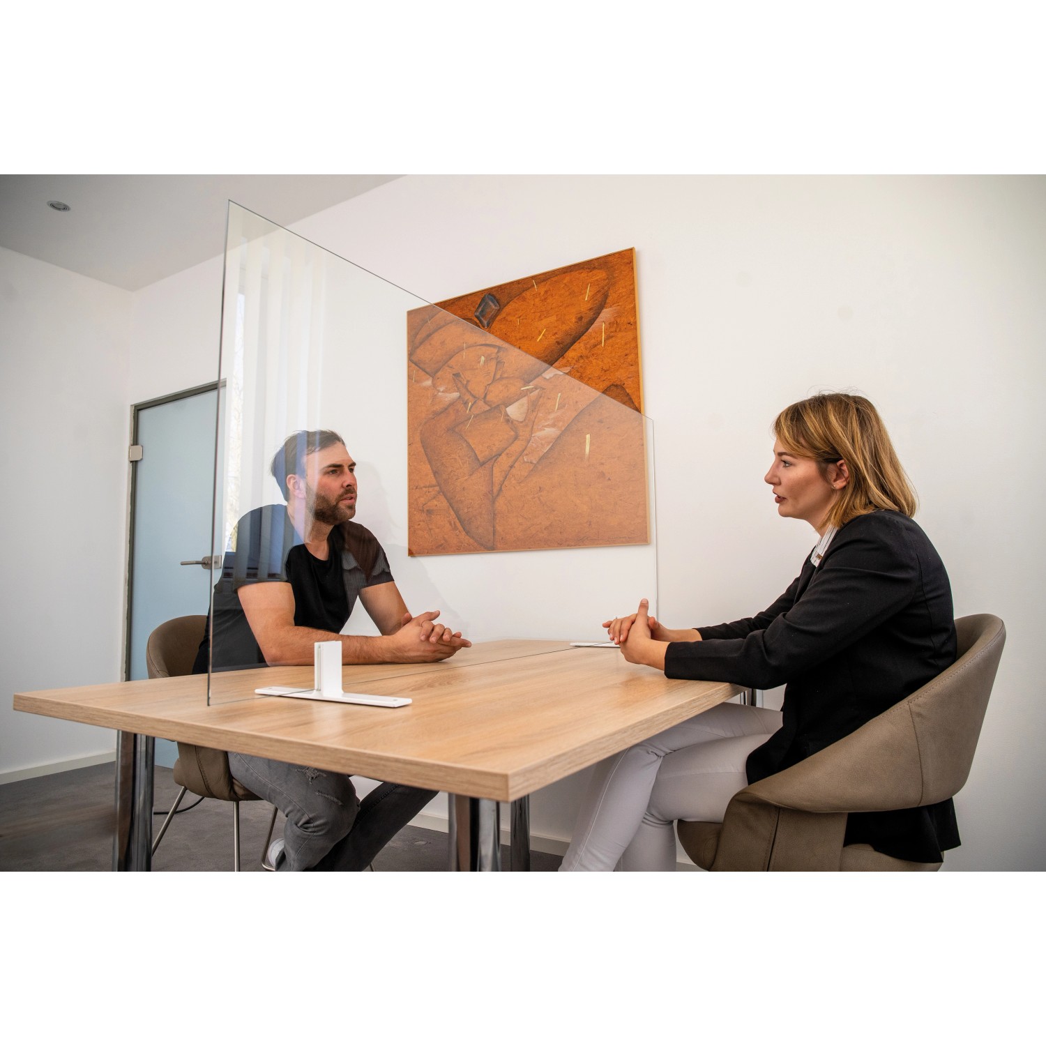 Hygiene Schutzglas (600x500x6 mm) als Spuckschutz zwischen zwei Personen an einem Tisch.