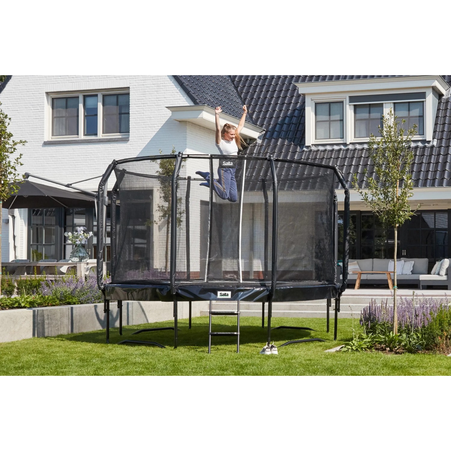 Schwarzes Salta Trampolin First Class (ø 487 cm) mit Sicherheitsnetz und Leiter im Garten.