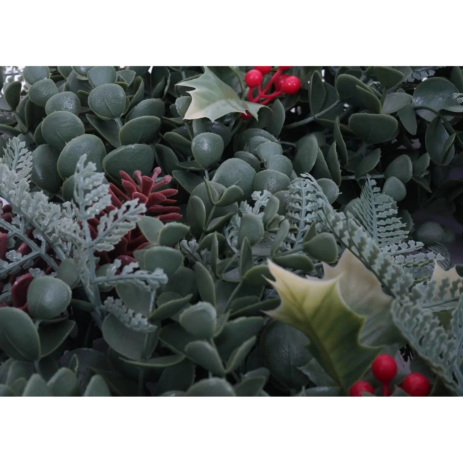 Detailansicht eines künstlichen Weihnachtskranzes mit grünen Blättern, roten Beeren und kleinen Zapfen.