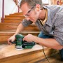 Mann schleift Holztreppe mit Bosch Exzenterschleifer PEX 400 AE. Schleifmaschine mit Staubabsaugung.