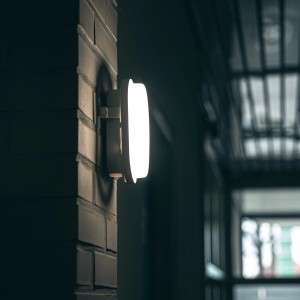 Weiße LED Außenwandleuchte, 1-flammig, montiert an einer Backsteinmauer.