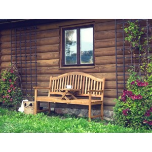 Helle Holzfarbene Beliani Gartenbank (150 cm) mit integriertem Tisch vor Holzwand.