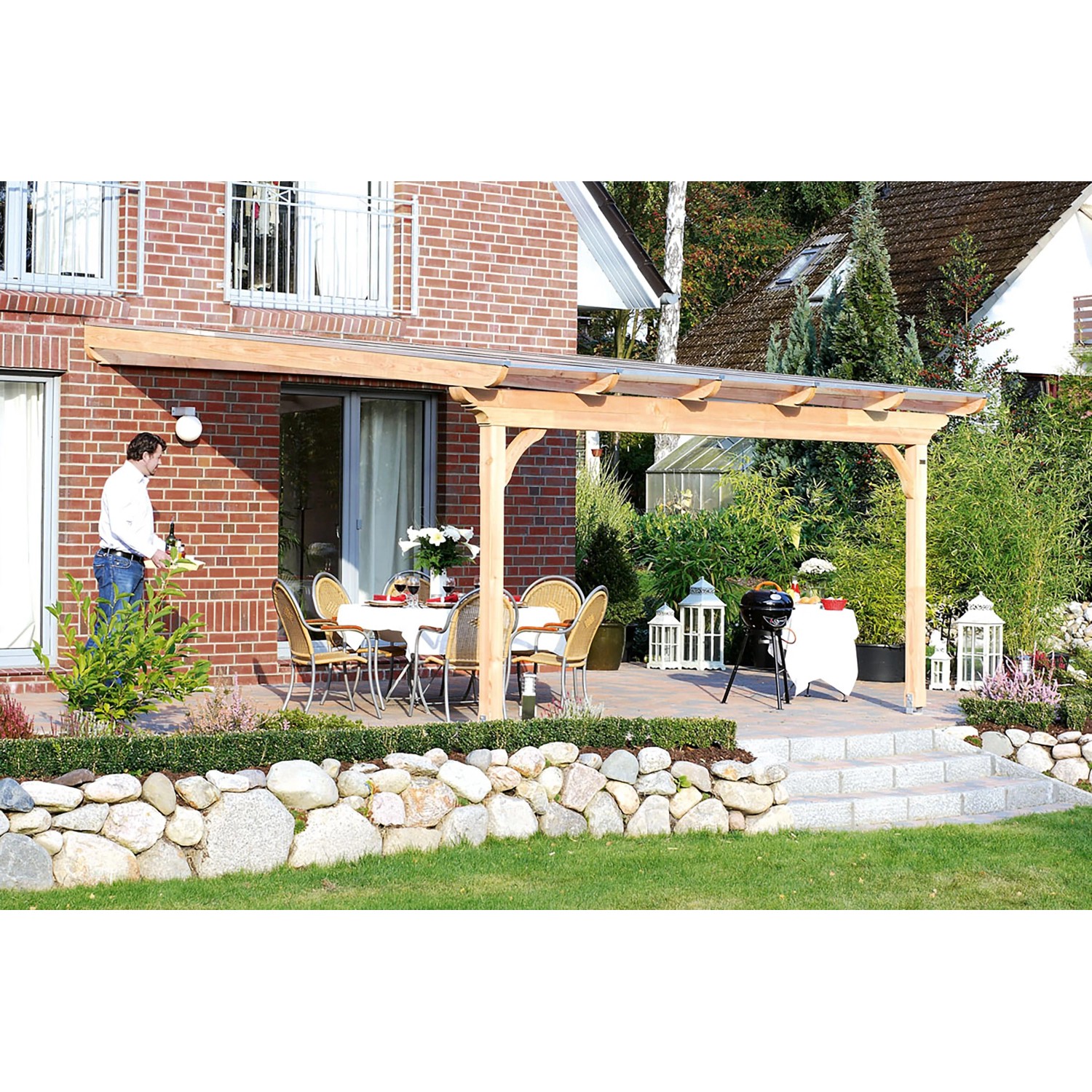 Skan Holz Terrassenüberdachung Ravenna aus hellem Douglasienholz mit transparentem Polycarbonatdach an Ziegelhaus.