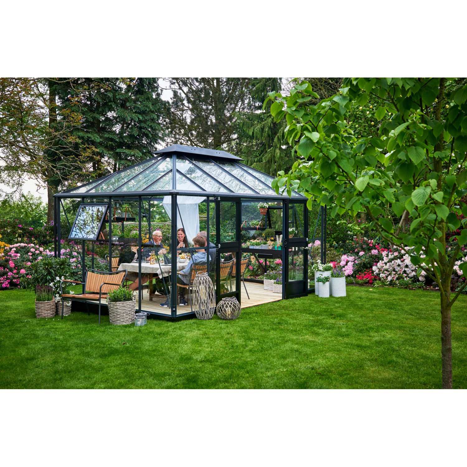 Juliana Gewächshaus Grand Oase 13 Anthrazit im Garten, mit Familie am Tisch. Begehbares Gewächshaus mit Aluminiumrahmen.