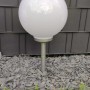 Dapo Solar Kugelleuchte Ola 25cm mit Erdspieß, weiße Kugel auf schwarzem Erdspieß im Garten.