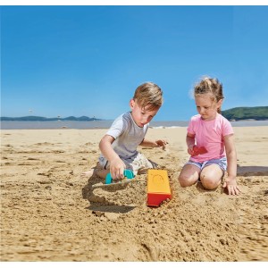 Kinder spielen mit Hape Sandspielzeug Maurermeister-Set am Strand. Mehrfarbiges 3-teiliges Set.