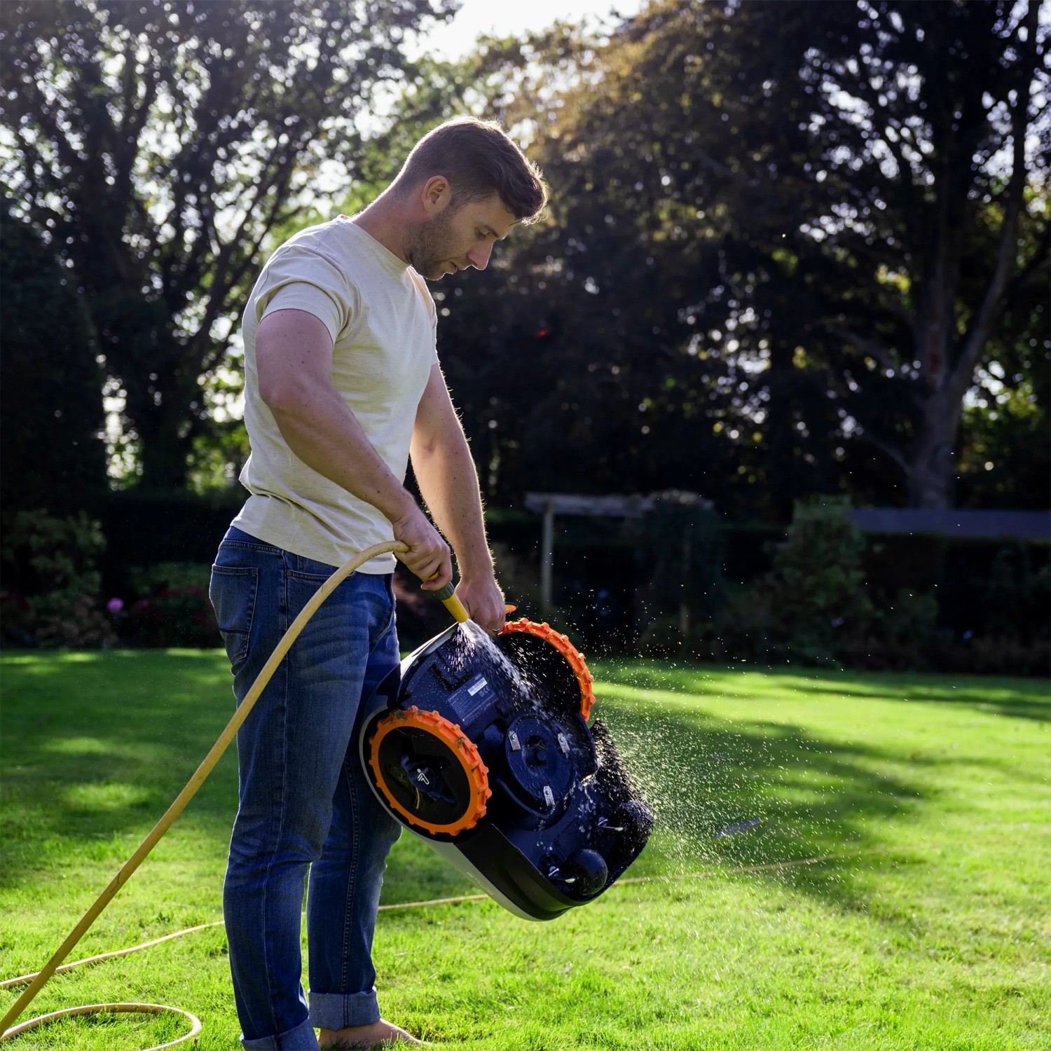 Mann reinigt Segway Navimow Mähroboter i105E mit Wasserschlauch im Garten.