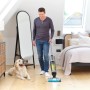Mann reinigt Holzboden mit Ryobi Multiflächenreiniger. Hund liegt daneben.