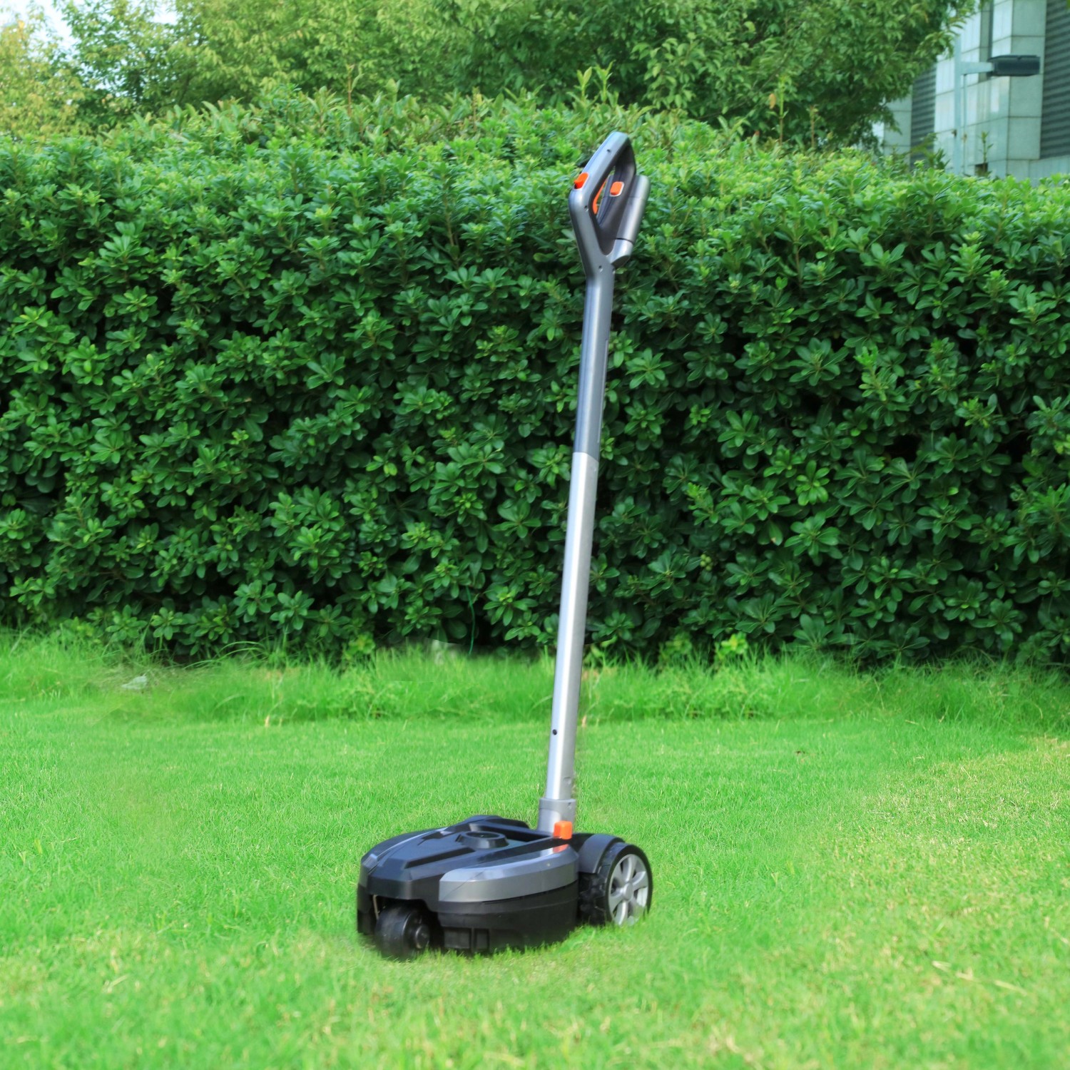 Yard Force Akku-Handmäher iFlex mit Rasentrimmeraufsatz auf Rasen vor grüner Hecke.