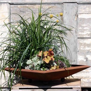Eckige Cortenstahl Blumenschale mit Edelrost-Patina, bepflanzt mit Gräsern und Blumen, auf Holzkiste.