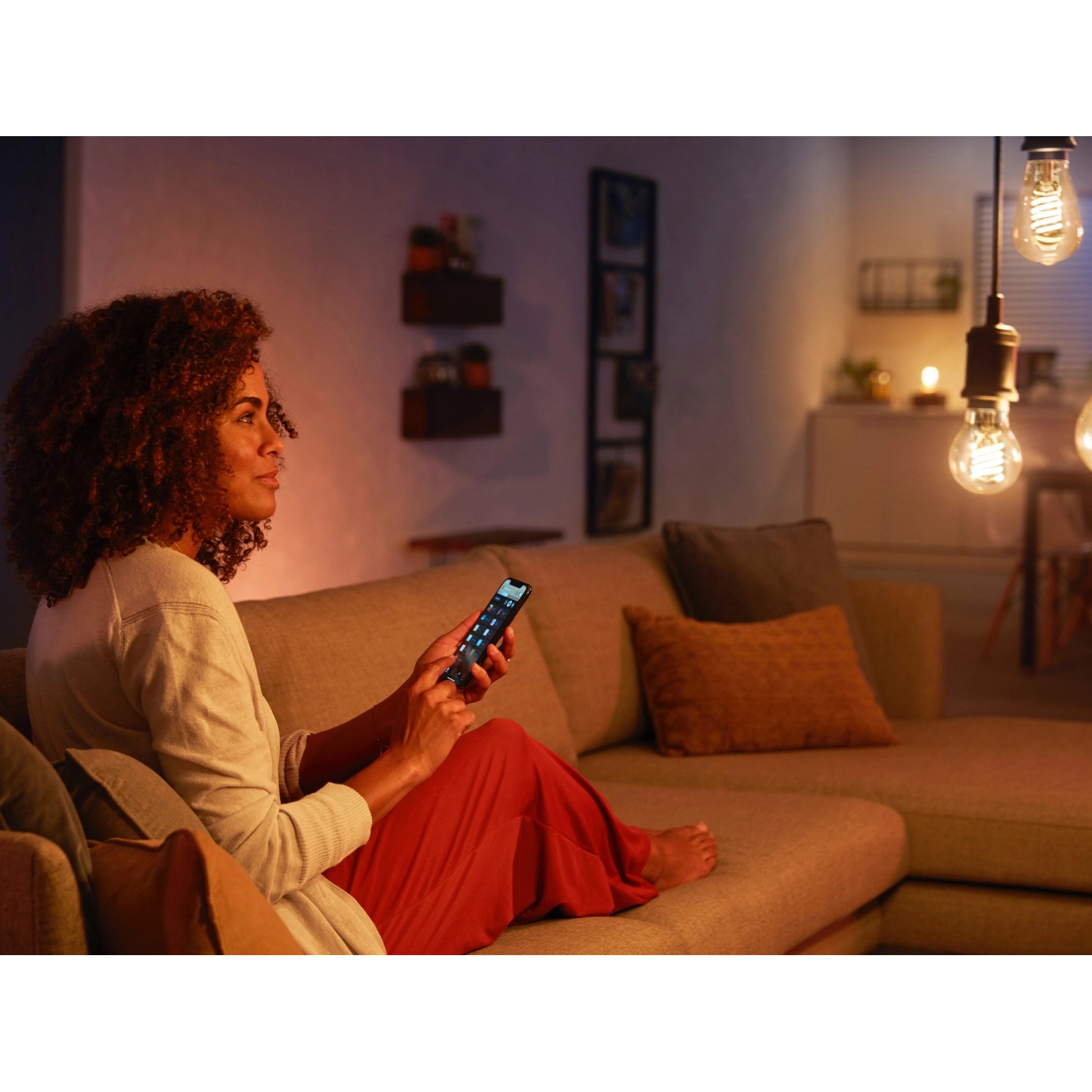 Frau dimmt Philips Hue Filament Lampe E27 mit dem Smartphone im Wohnzimmer.