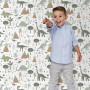 Fröhlicher Junge vor ESTAhome Vliestapete mit Vintage Dinosauriern, Bäumen und Bergen in Blau/Grün für Kinderzimmer.