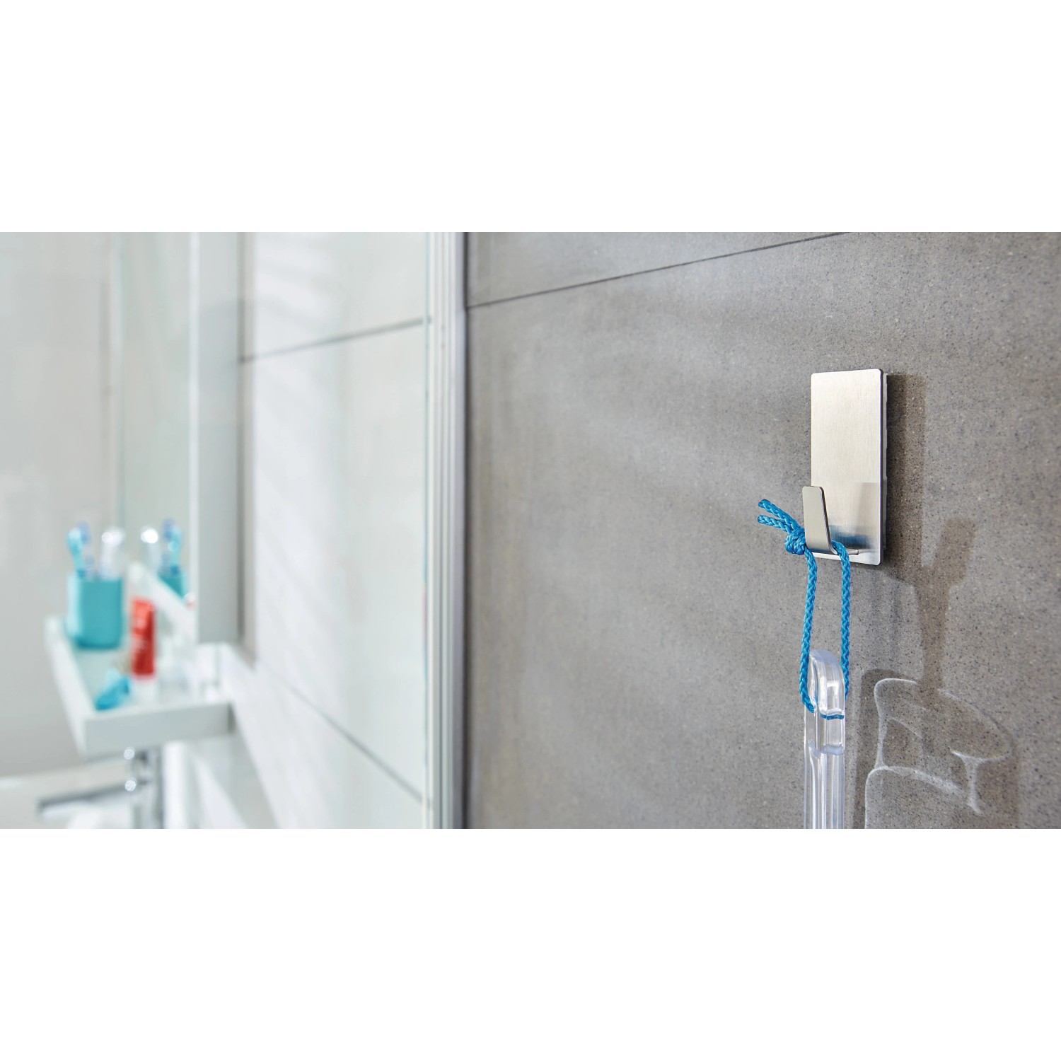 Tesa Powerstrips Haken Waterproof eckig Edelstahl Large an grauer Wand mit aufgehängtem Gegenstand.