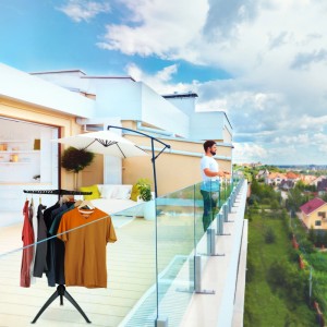 Schwarz-grauer klappbarer Bügelwäscheständer mit Kleidung auf Balkon. Zum Wäsche trocknen & lüften.