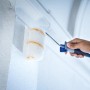 LUX Dispersionsroller 15 cm im Einsatz: Hand streicht weiße Wand mit Farbwalze.