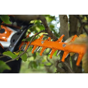 Stihl Akku-Heckenschere HSA 130 T mit orangefarbenen Messern schneidet präzise Äste einer Hecke.