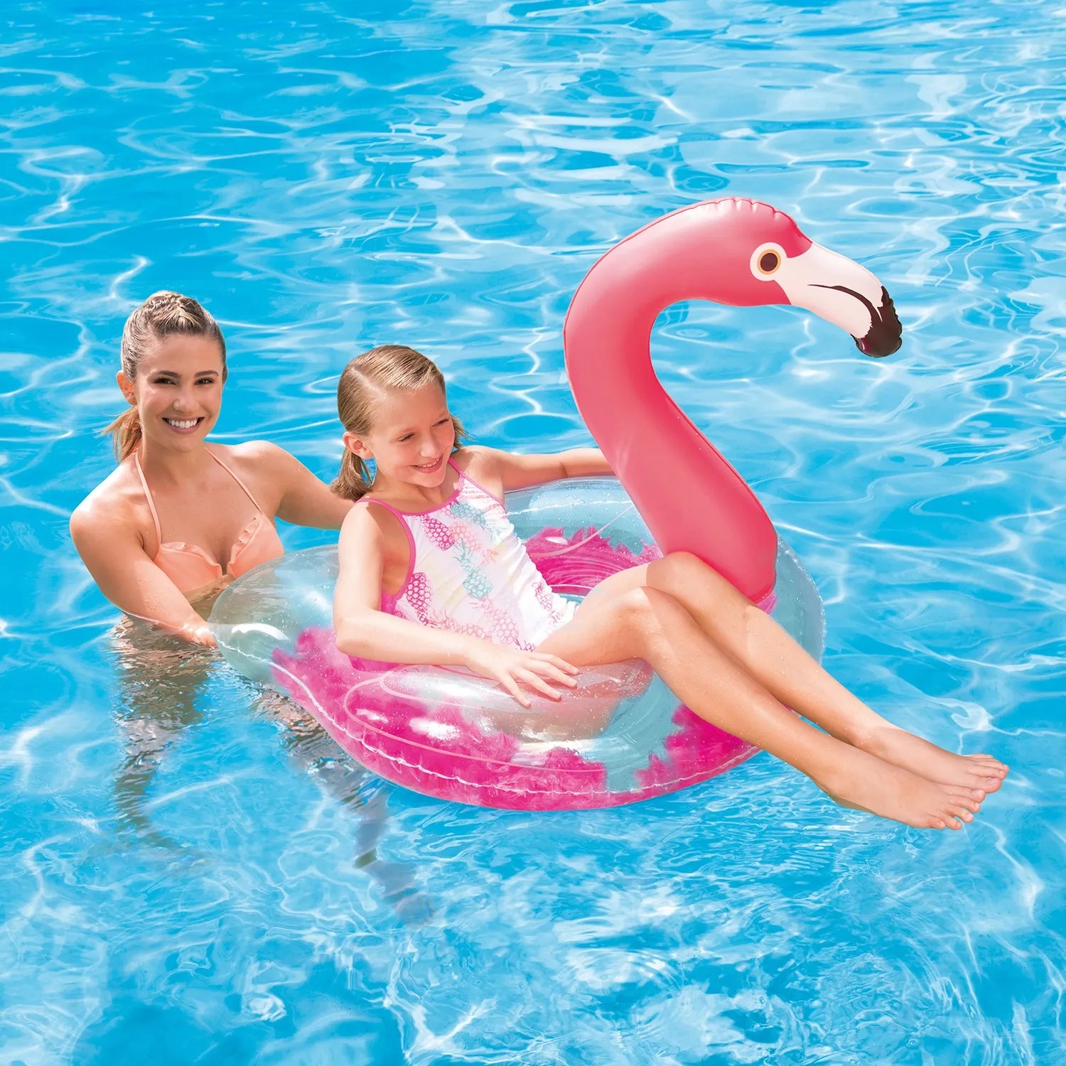 Mädchen sitzt im Schwimmring Flamingo (107x80cm) im Pool, eine Frau steht daneben.