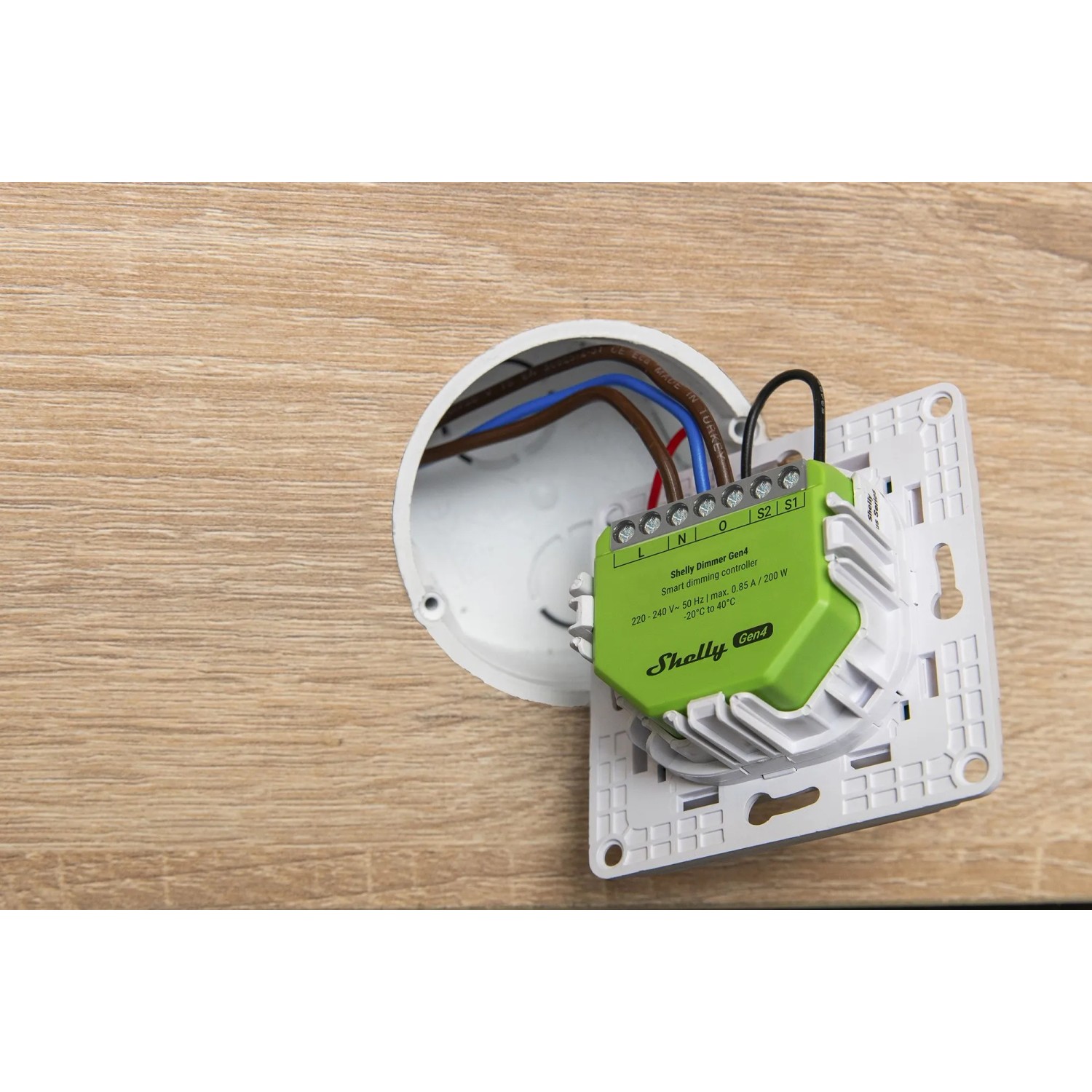 Grüner Shelly Smarte Relais Dimmer Gen 4 für Hausautomation, installiert in einer Wanddose.