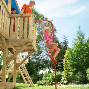 Kind rutscht rote Winnetoo Feuerwehrstange an Spielturm im Garten hinunter.